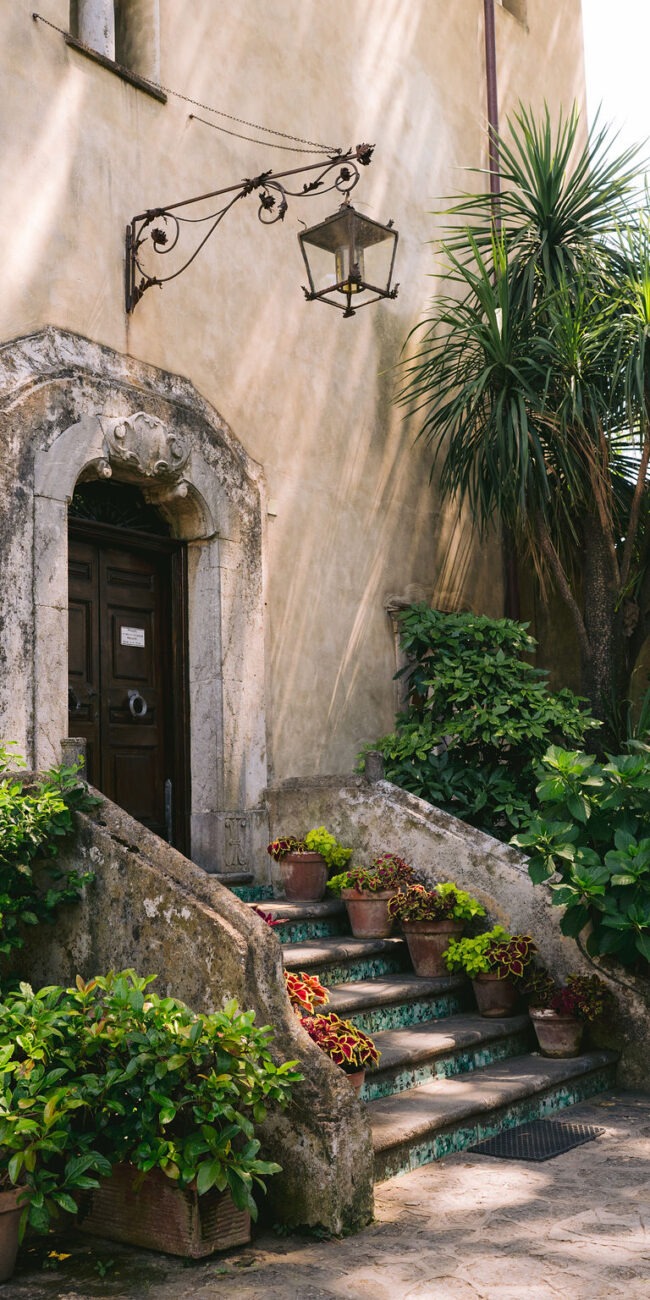 An elegant stone access door with arched details surrounded by lush greenery and steps at Villa Cimbrone.