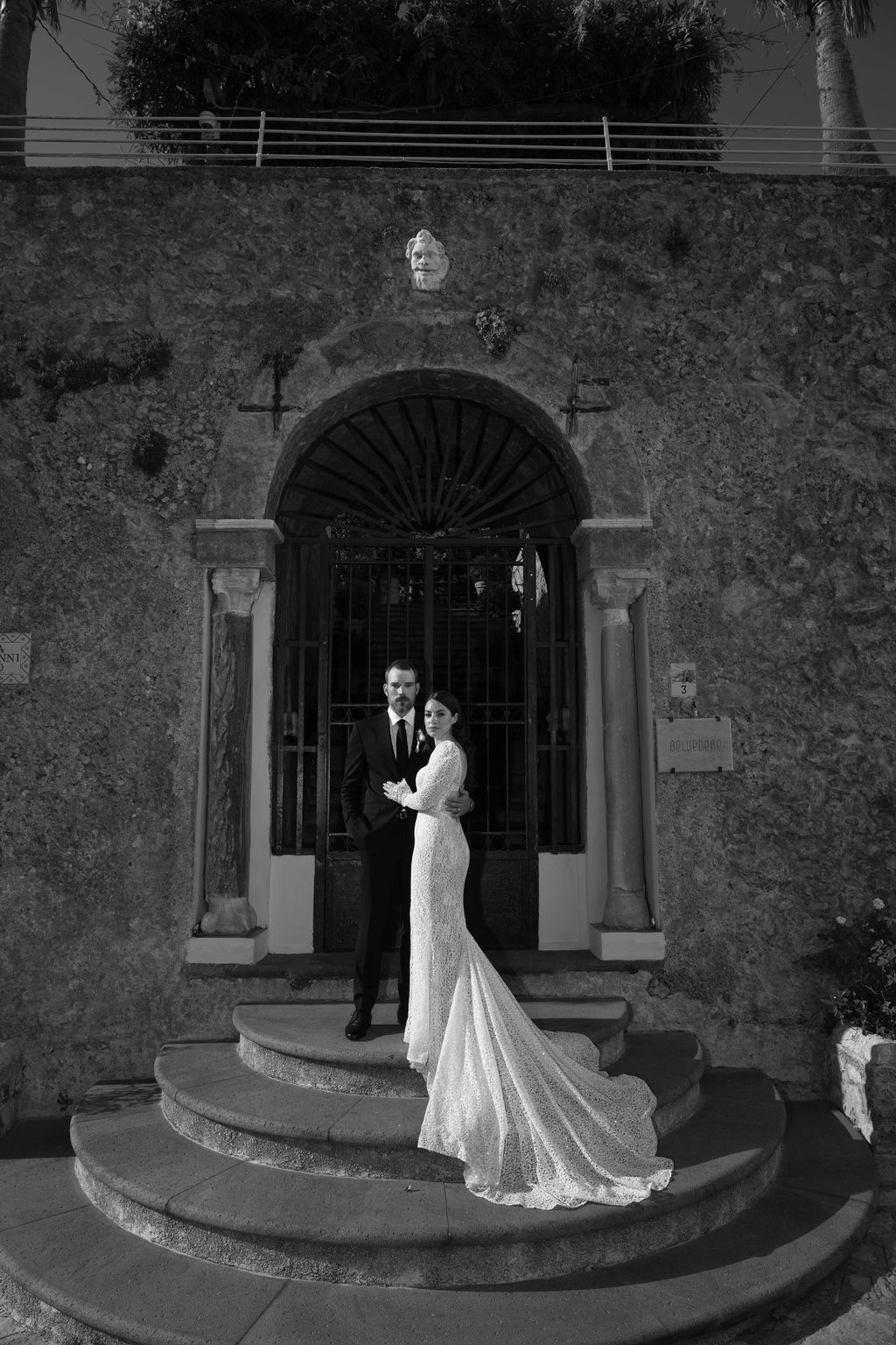 Black and white photo of a bride and groom standing on the steps of a grand arched doorway at Villa Cimbrone.