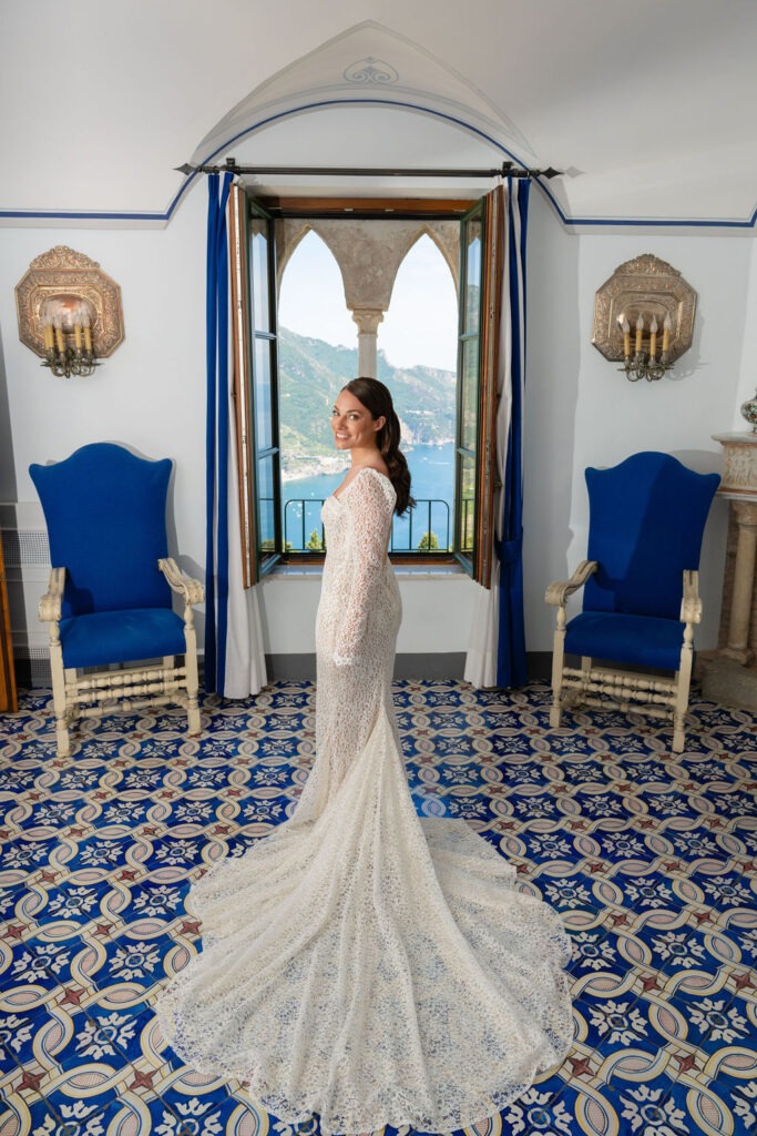 A bride in a luxurious white gown standing in an elegant room with blue chairs and a tiled floor at Villa Cimbrone.