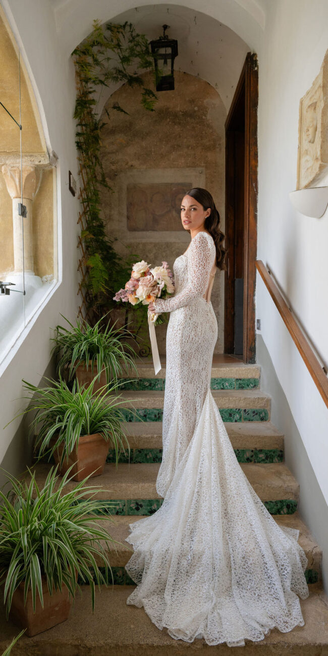 A bride in a stunning white gown standing on an elegant staircase adorned with greenery at Villa Cimbrone.