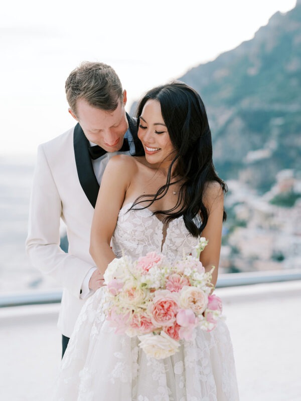 Bride and groom smiling closely, holding a delicate pastel bouquet.