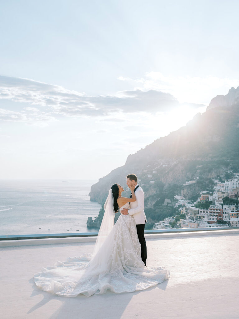 Bride and groom embracing with a stunning coastal view at sunset.